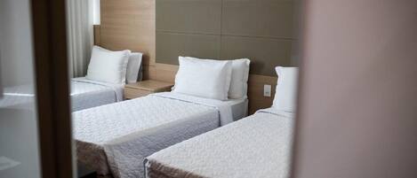 A hotel room with three single beds, each with a wooden headboard and white bedding.