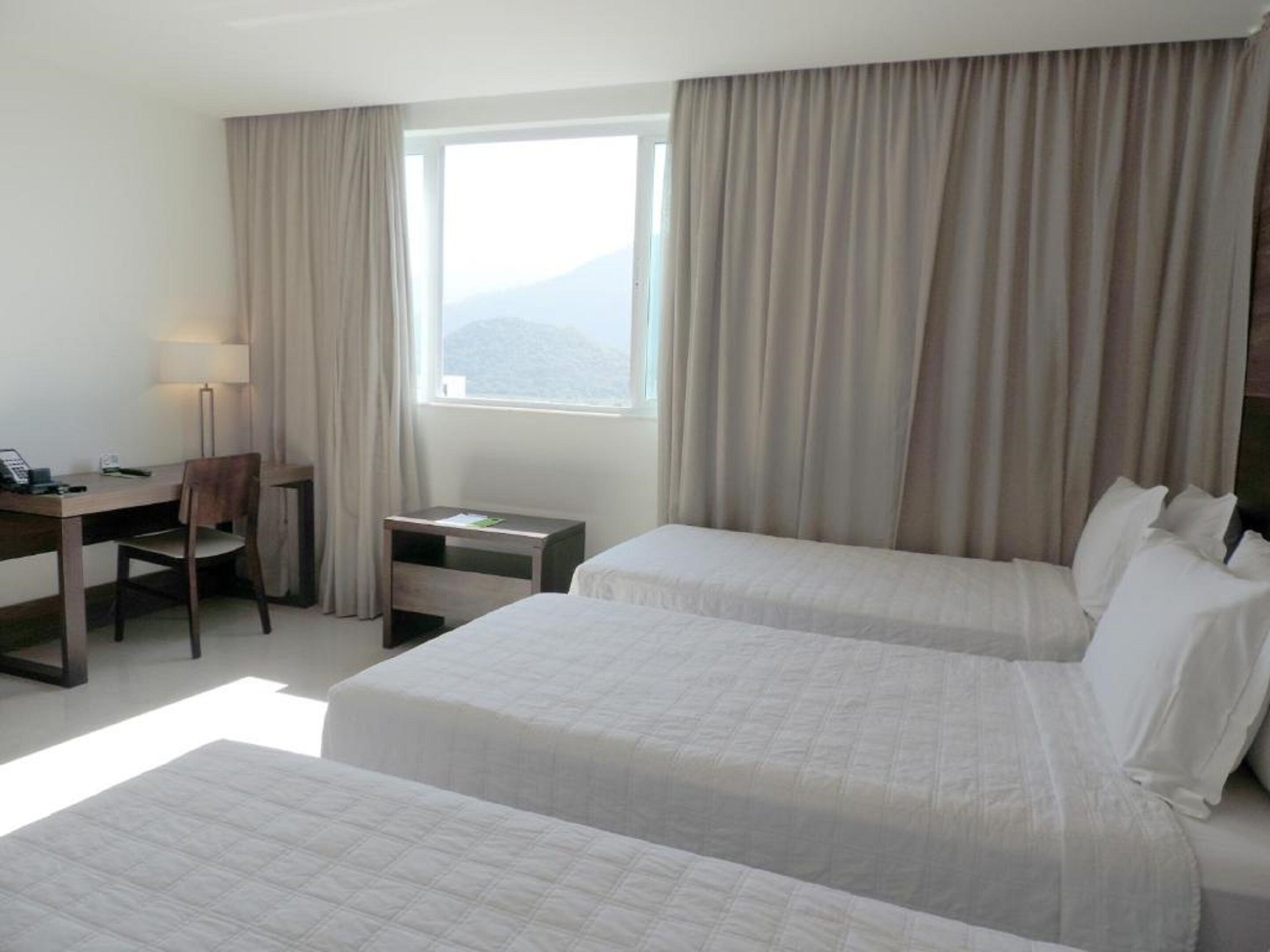 A hotel room with two beds, a desk, a chair, a small table, and a window with curtains.