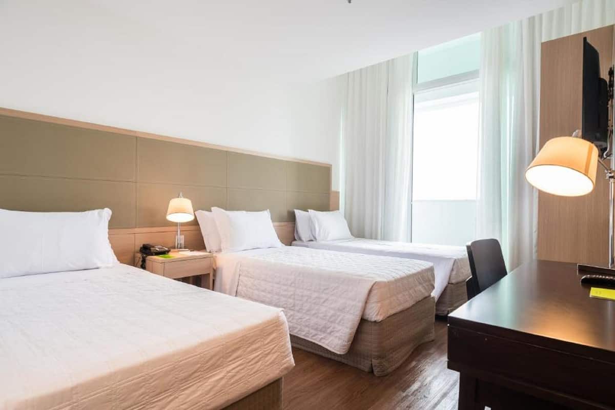 A hotel room with two beds, a desk, a chair, and a large window with curtains.