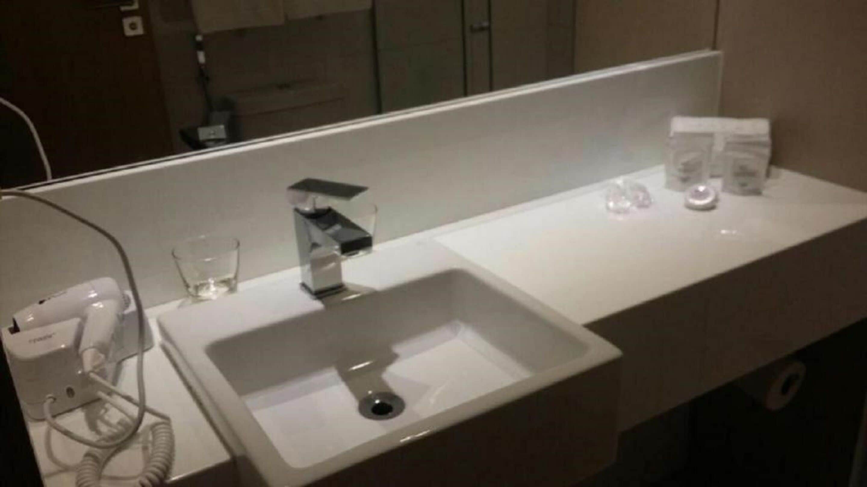 Une salle de bain d’hôtel avec un lavabo blanc, un miroir, un verre et un téléphone.