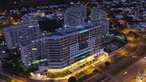 Um hotel com vários andares e uma placa grande com a inscrição 'AMÉRICAS', rodeado por outros edifícios e uma rua bem iluminada.