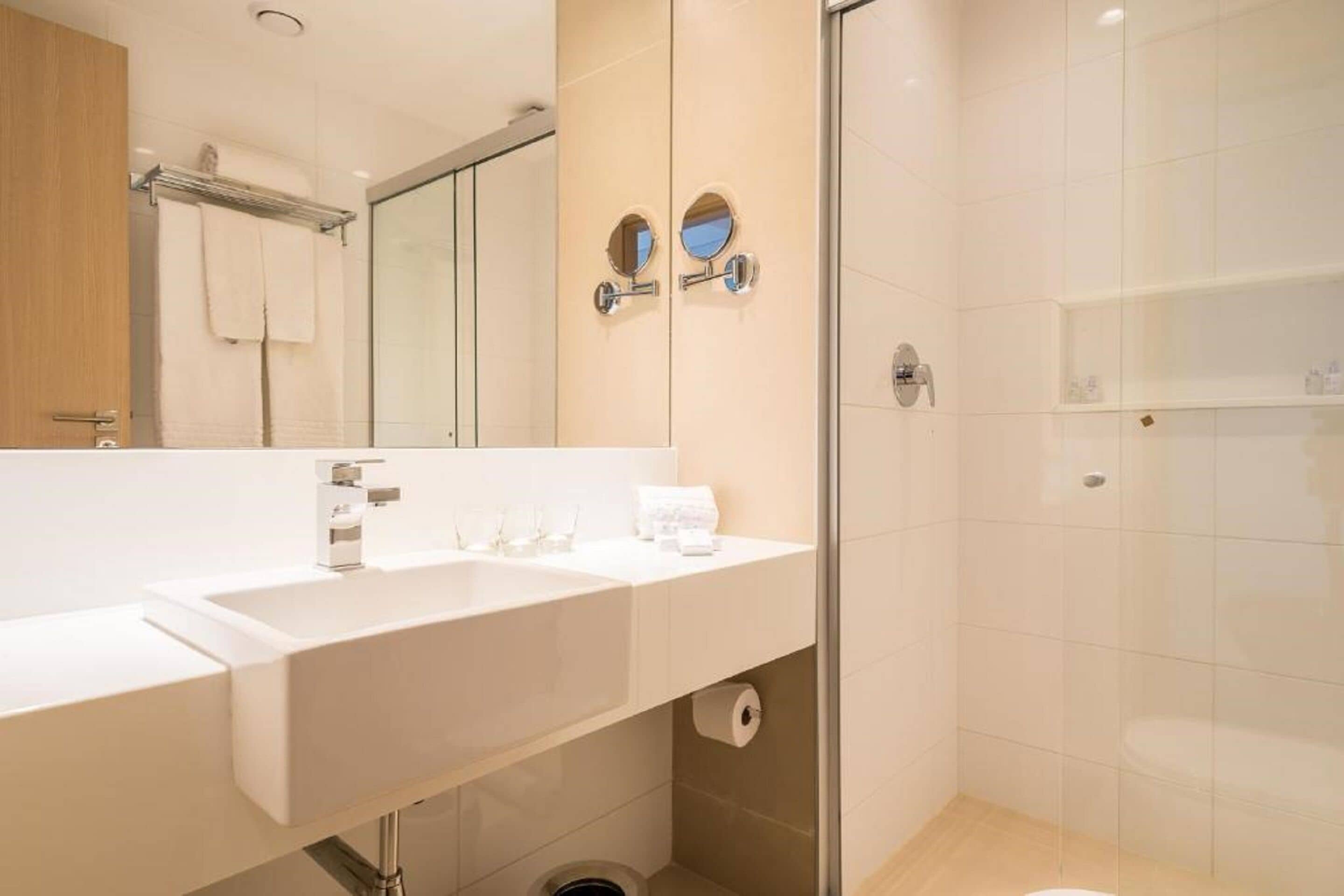 A modern bathroom with two sinks, a mirror, and a shower area.