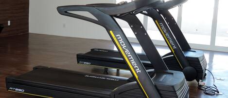 Two treadmill exercise machines with the brand name 'Movement' and model 'RT250' in a room with wooden flooring and a large window.