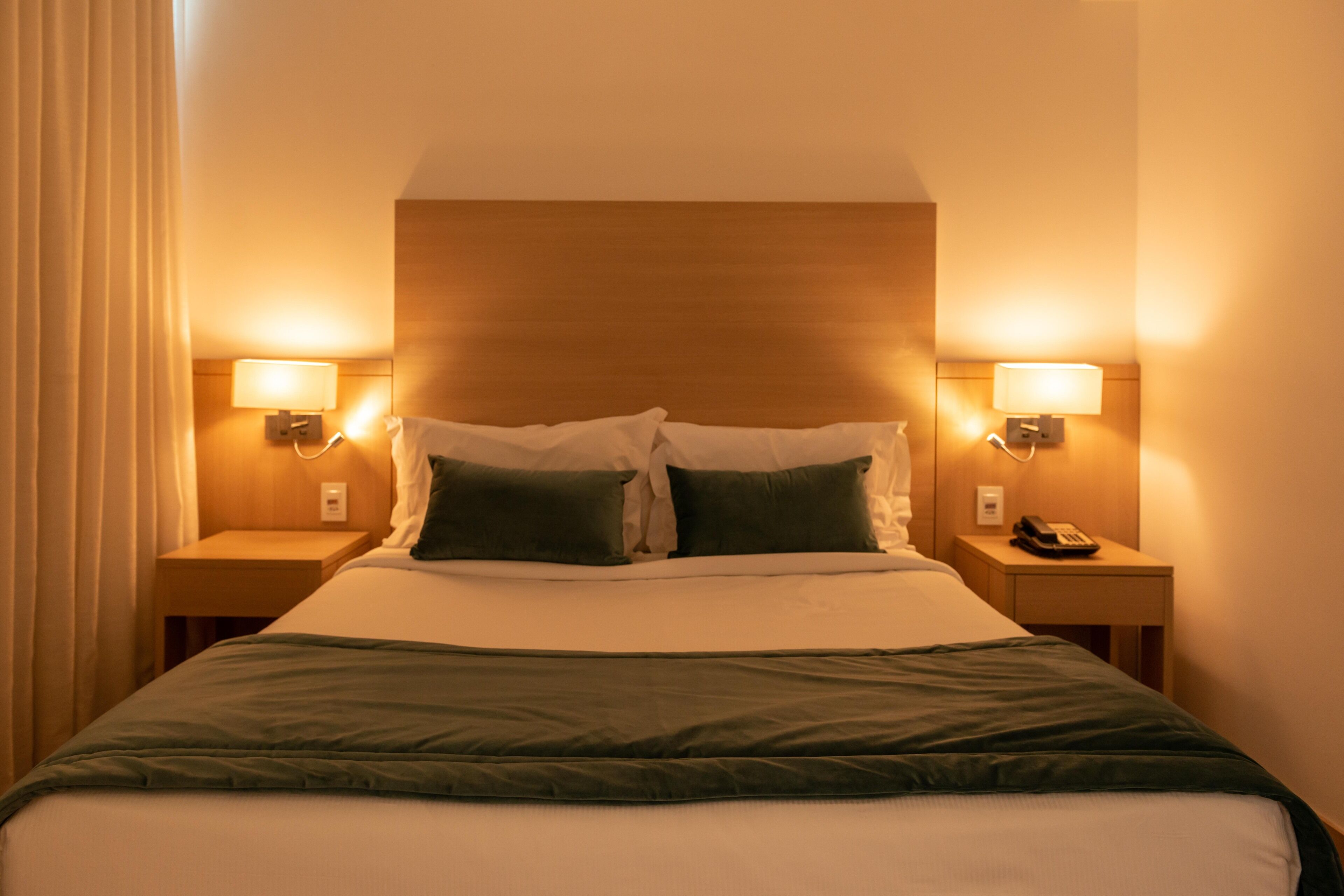 A hotel room with a large bed, two bedside lamps, a nightstand with a telephone, and a wooden headboard.