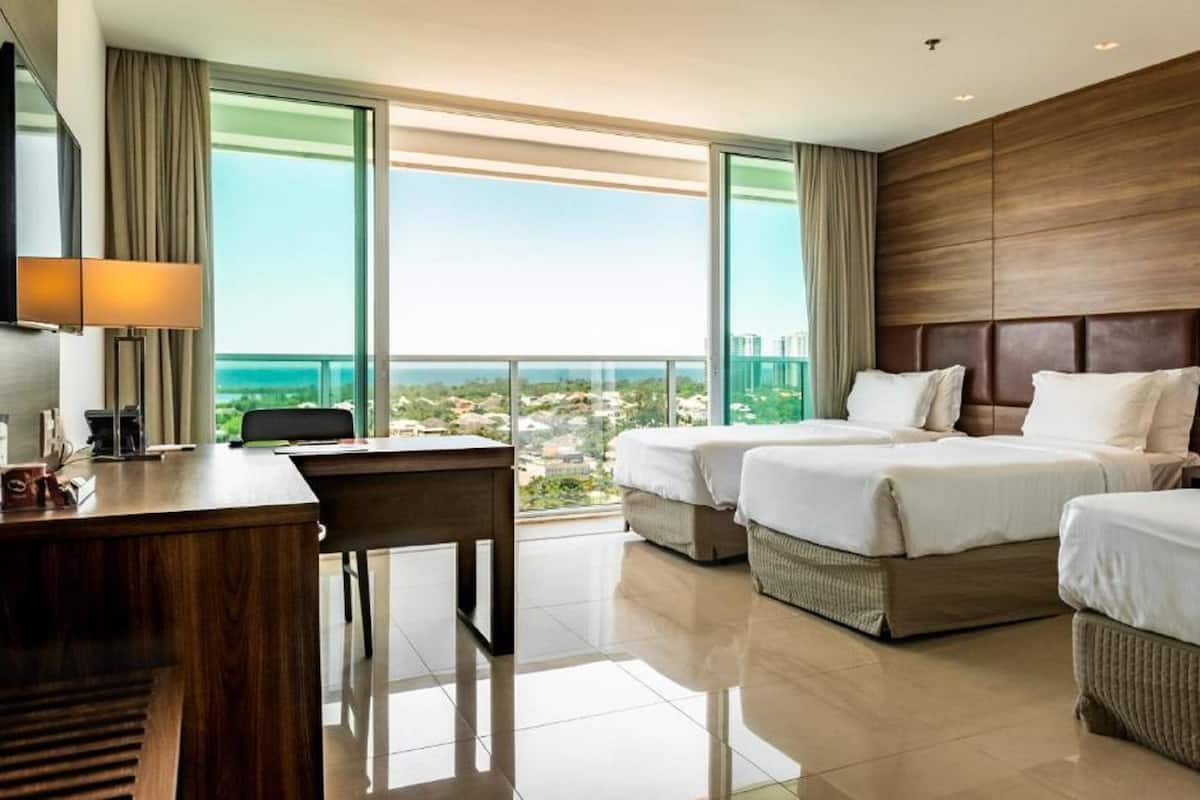A hotel room with two beds, a desk, and a view of the city.