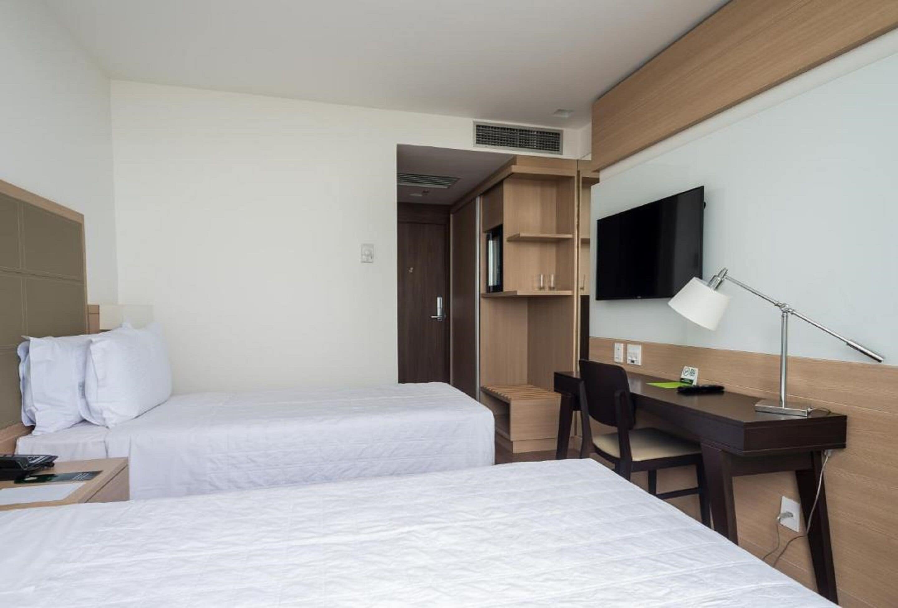 Une chambre d’hôtel avec deux lits, un bureau, une chaise, une télévision et une lampe.