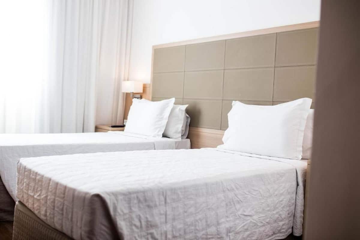 Two single beds with white linens in a hotel room.