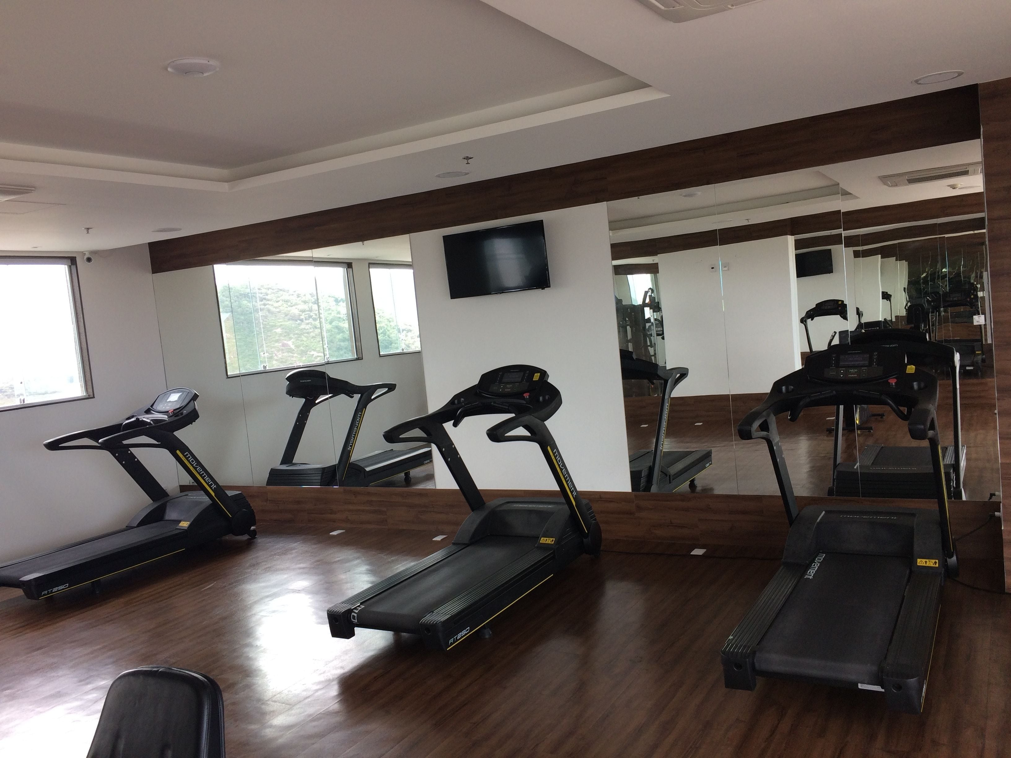 A gym with multiple treadmills, a large mirror, and a TV on the wall.