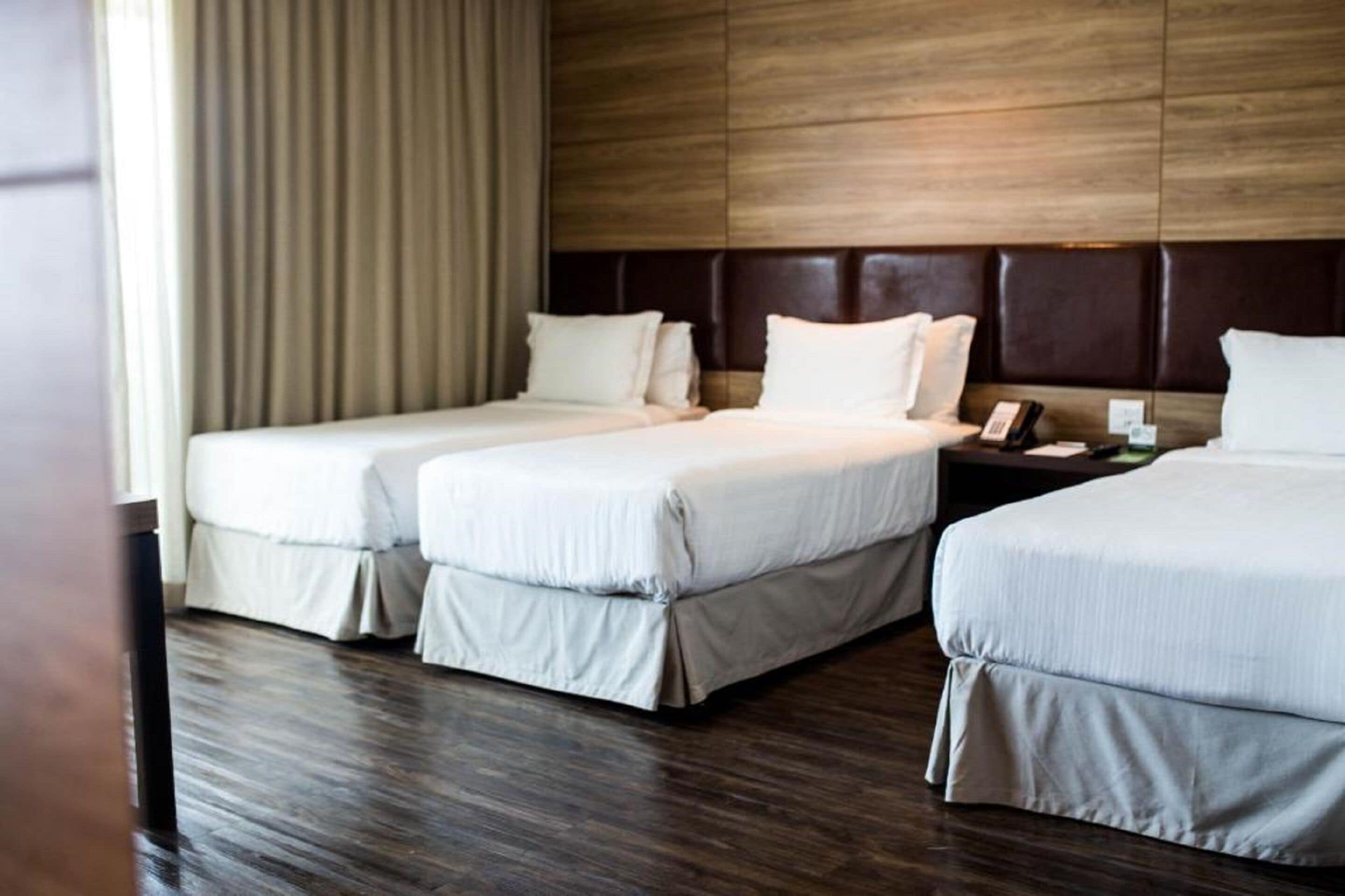 Habitación de hotel con dos camas, un cabecero de madera, una mesita de noche con teléfono y una ventana con cortinas.