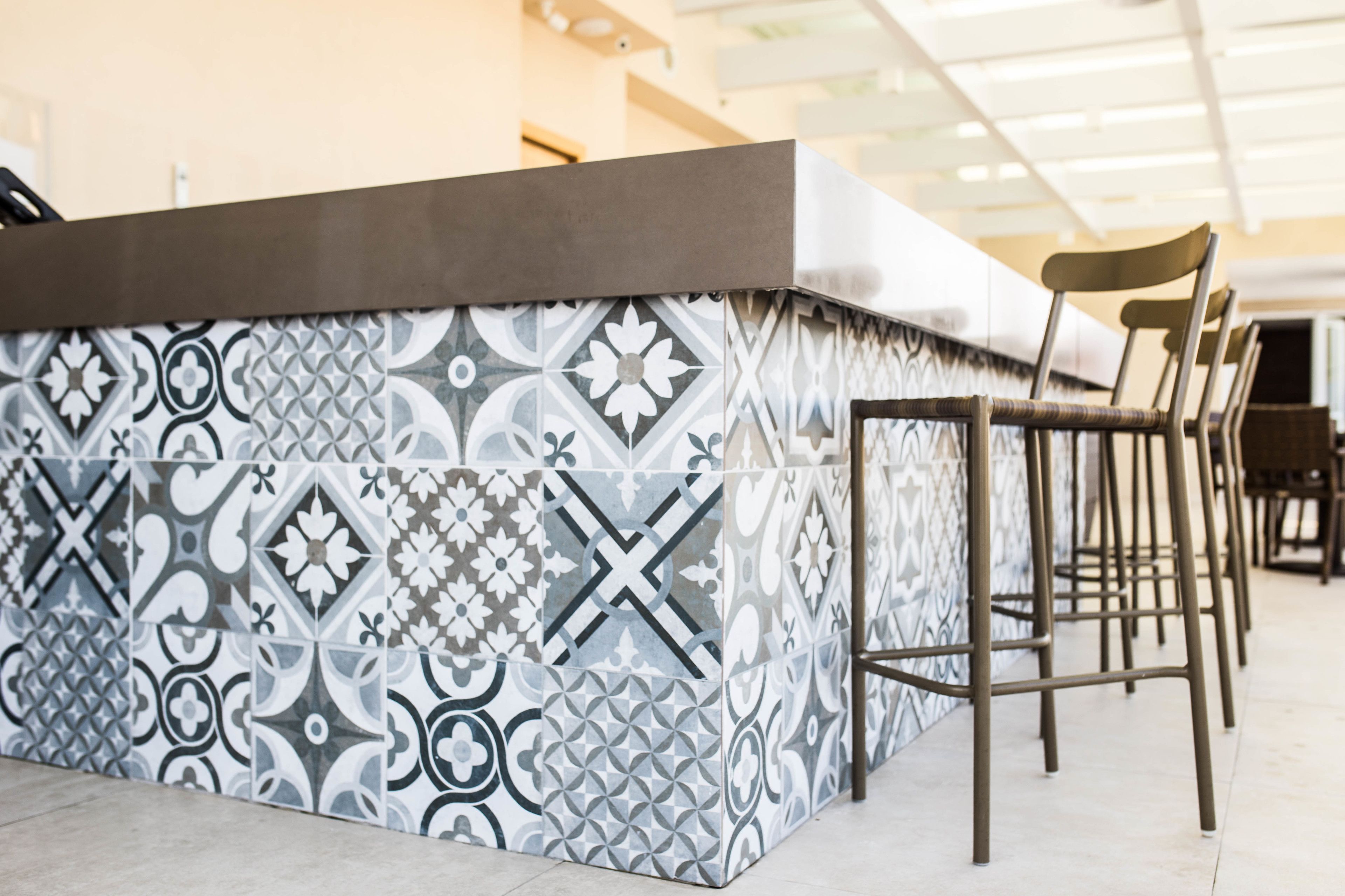 A bar area with a patterned tile wall and metal bar stools.