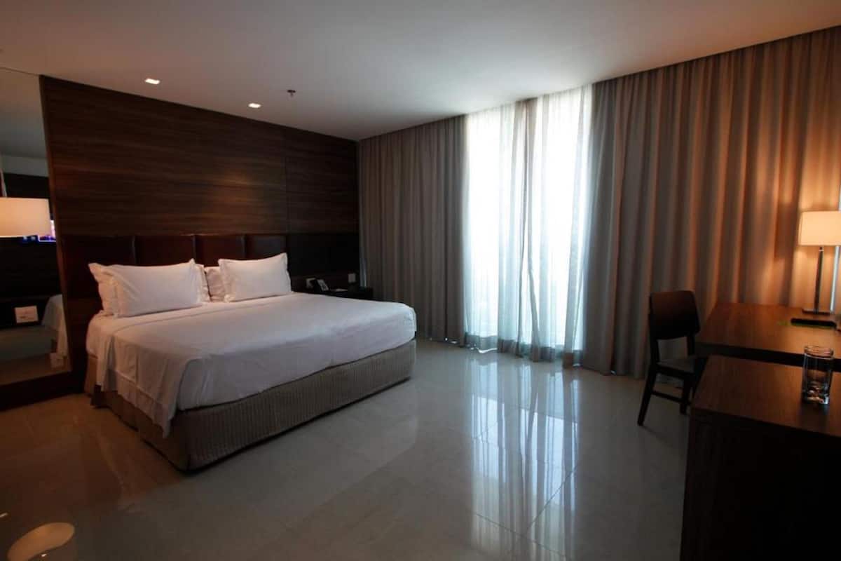 A modern hotel room with a large bed, a desk, and a chair.