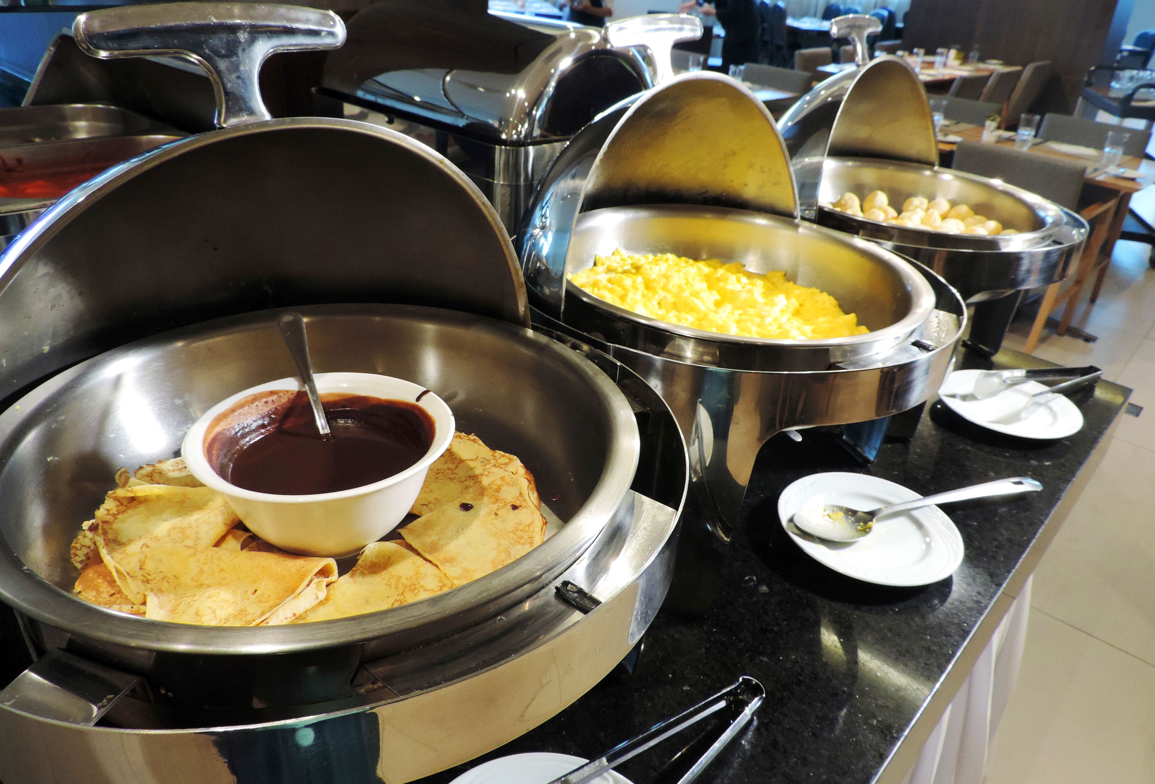 A buffet with various food items including crepes, a chocolate sauce bowl, and a bowl of scrambled eggs.