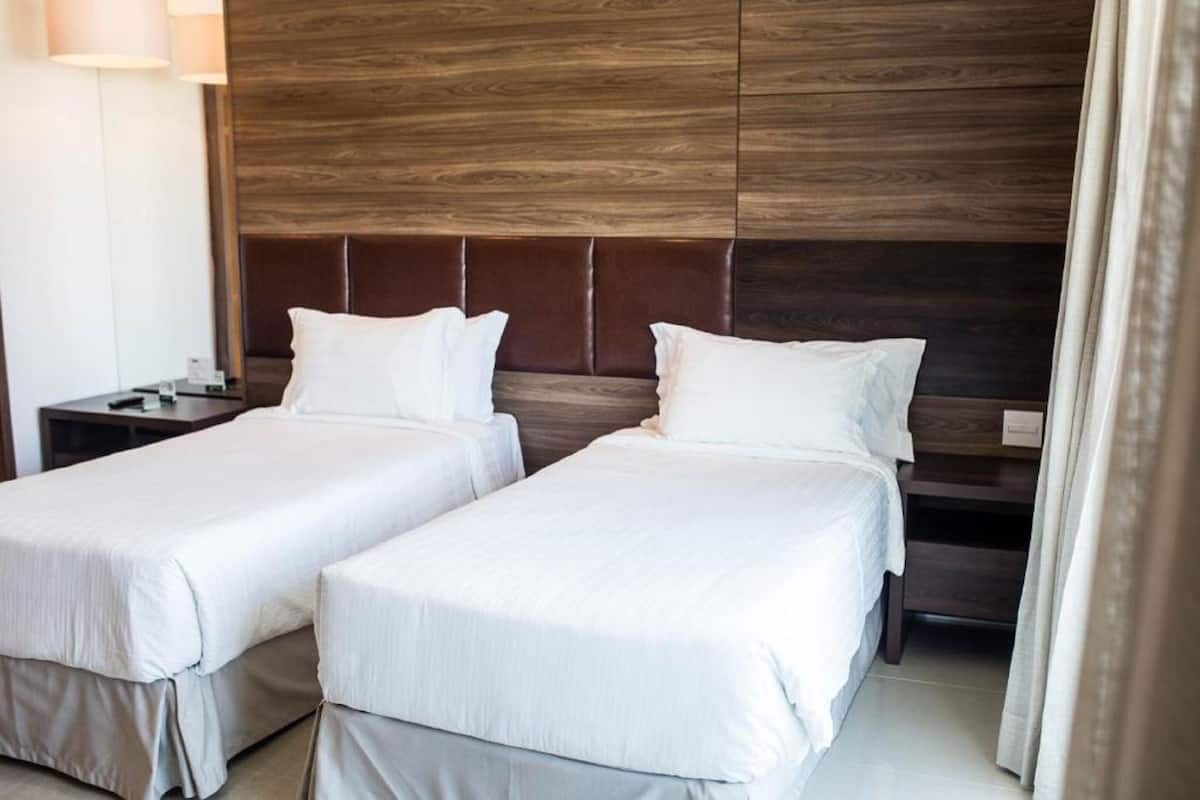A hotel room with two beds, a wooden headboard, and a nightstand with a lamp.