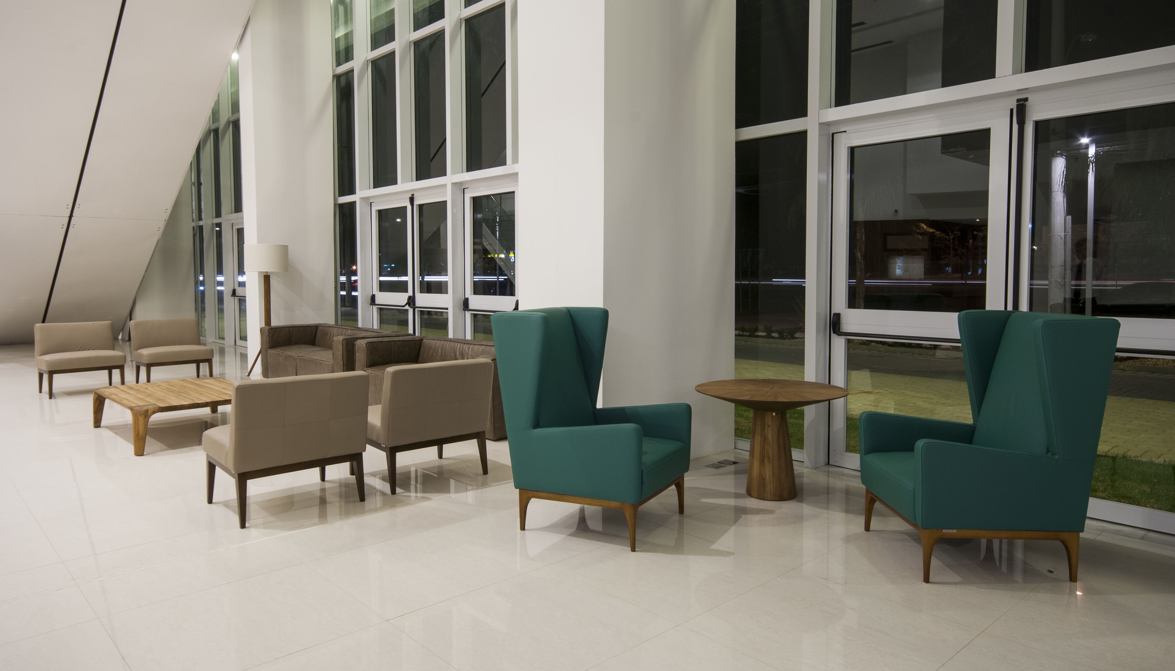 A modern interior with a seating area featuring sofas and armchairs, large windows, and a tiled floor.