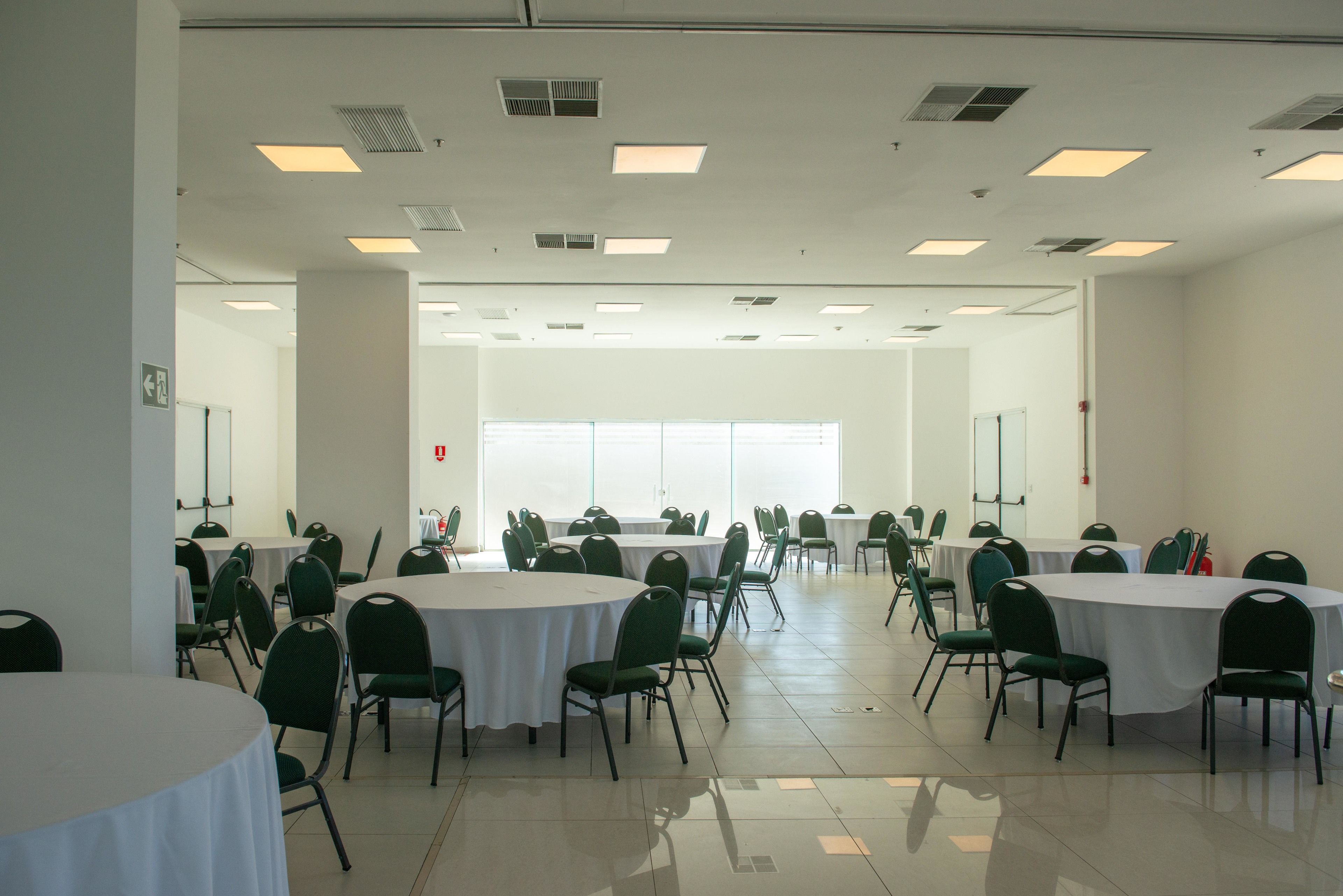 Una sala conferenze con tavoli rotondi multipli e sedie verdi, pareti bianche e ampie finestre.