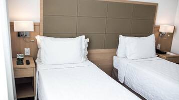 Une chambre d’hôtel avec deux lits simples, une tête de lit en bois, des lampes de chevet, une table de chevet avec un téléphone et une horloge, et un interrupteur fixé au mur.