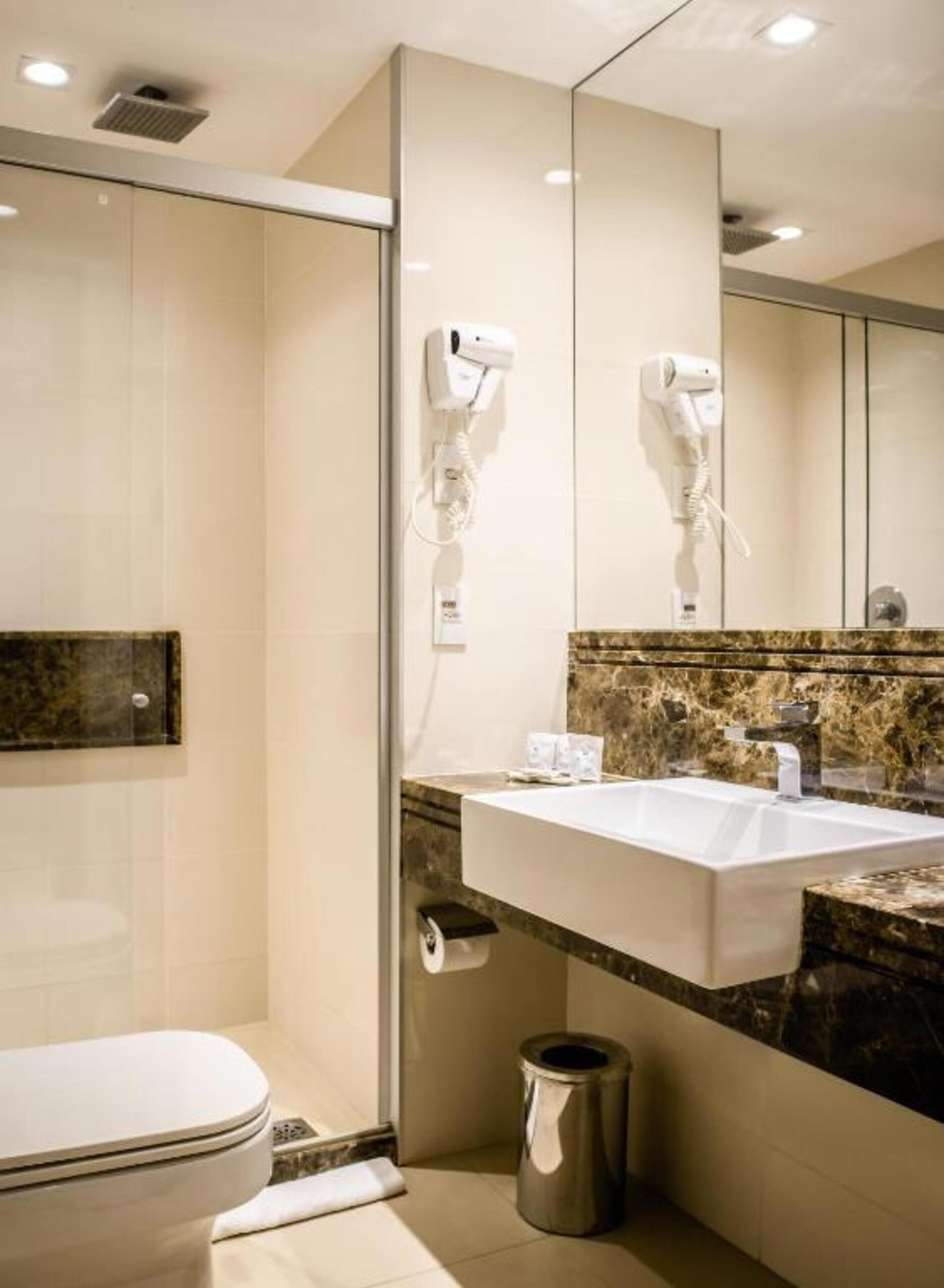 Un baño moderno con un lavamanos blanco, un espejo y dos secadores de pelo fijados en la pared.