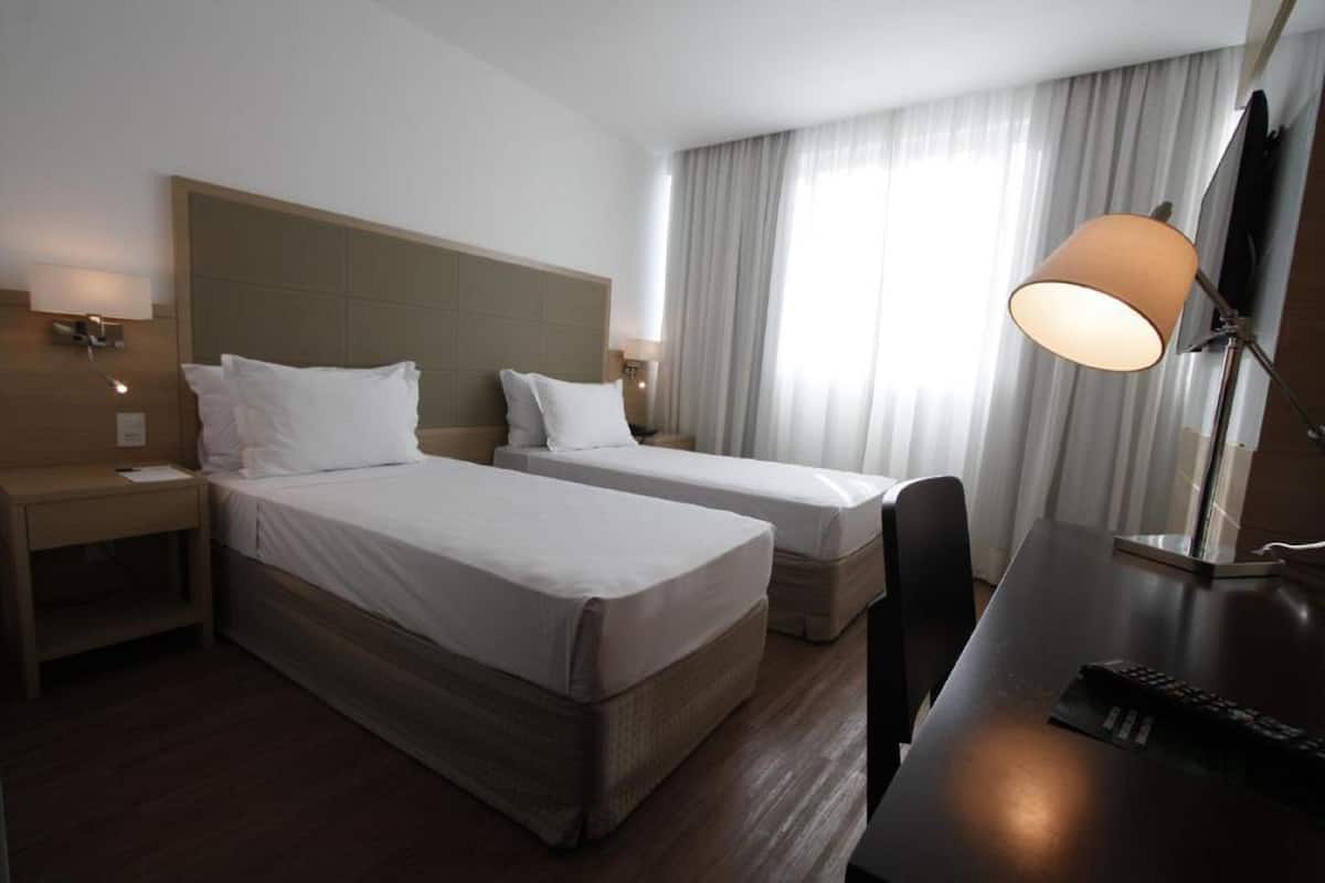 A hotel room with two single beds, a desk with a lamp, and a TV.