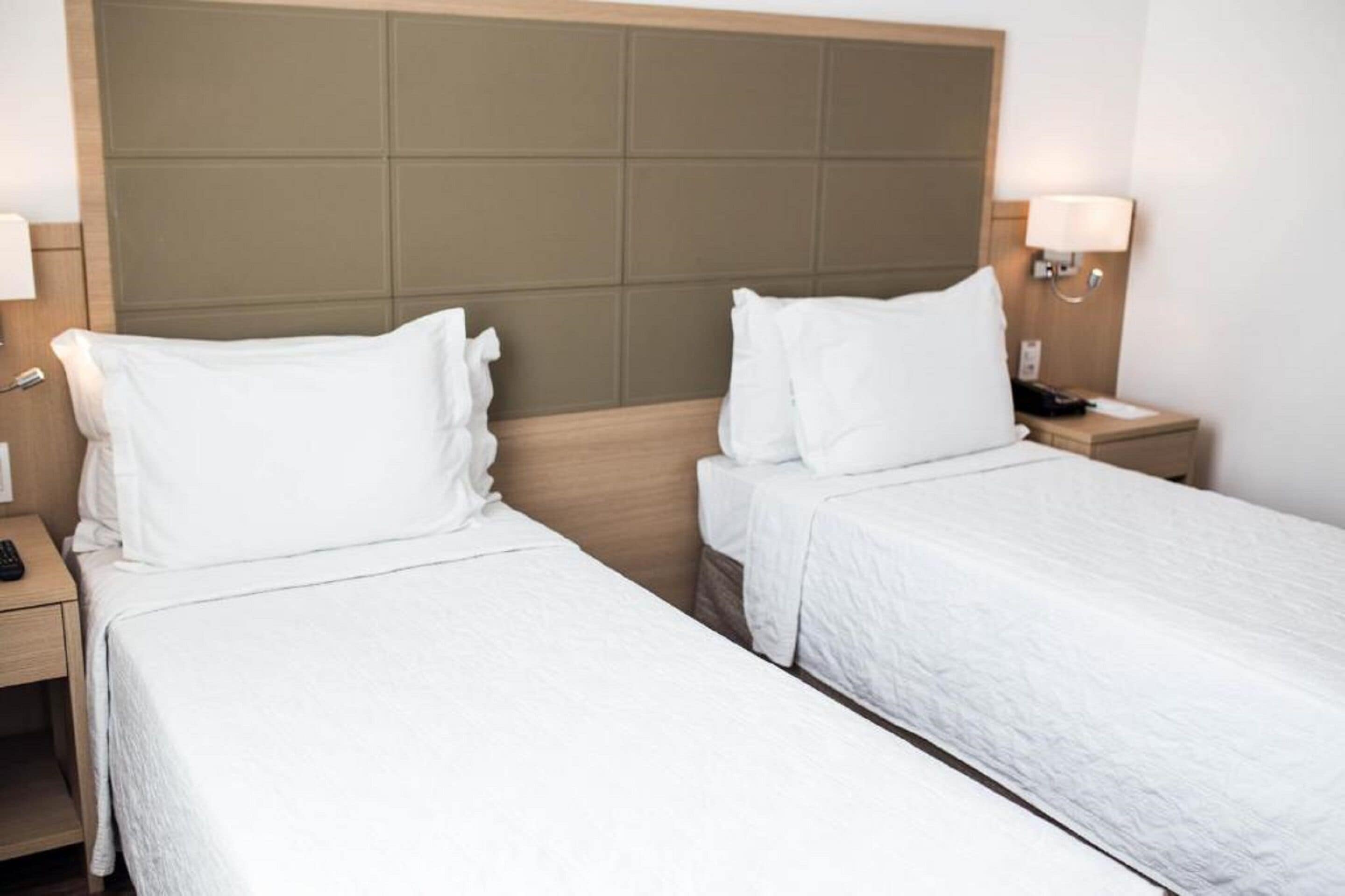 Een hotelkamer met twee enkele bedden, een houten hoofdbord, bedlampen en een nachtkastje met een telefoon.