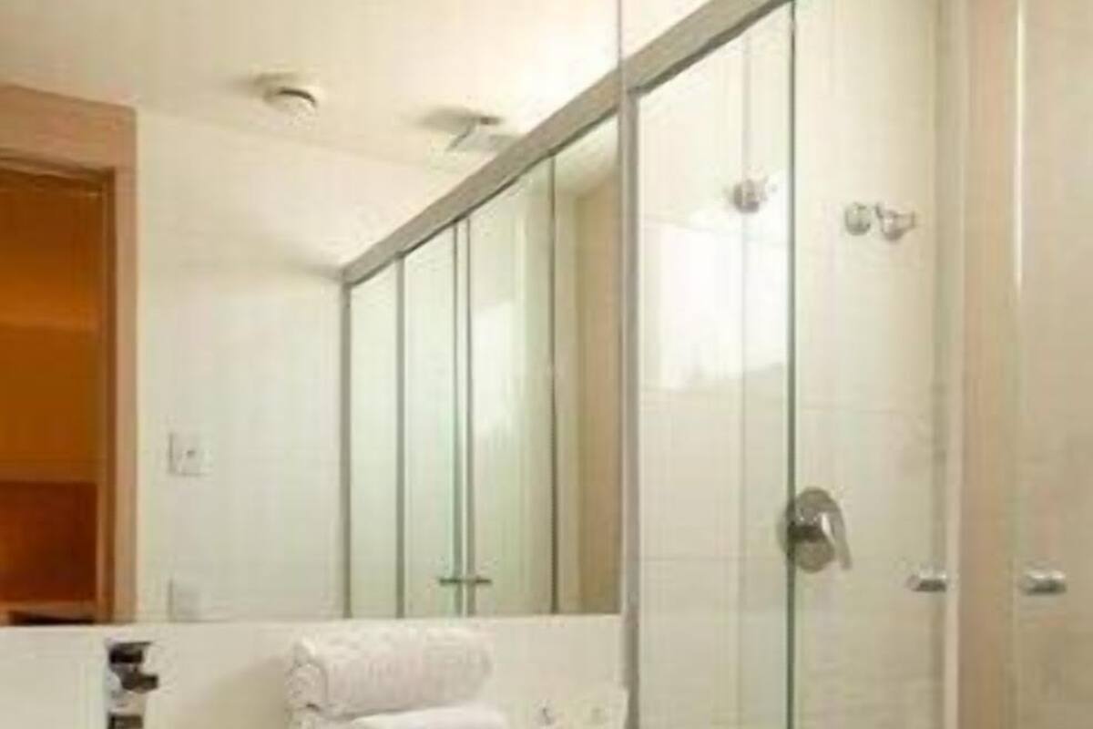 A modern bathroom with a glass shower enclosure, a white sink, and a trash can.