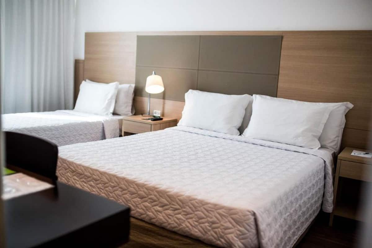 A hotel room with two beds, a nightstand with a lamp, and a desk with a chair.