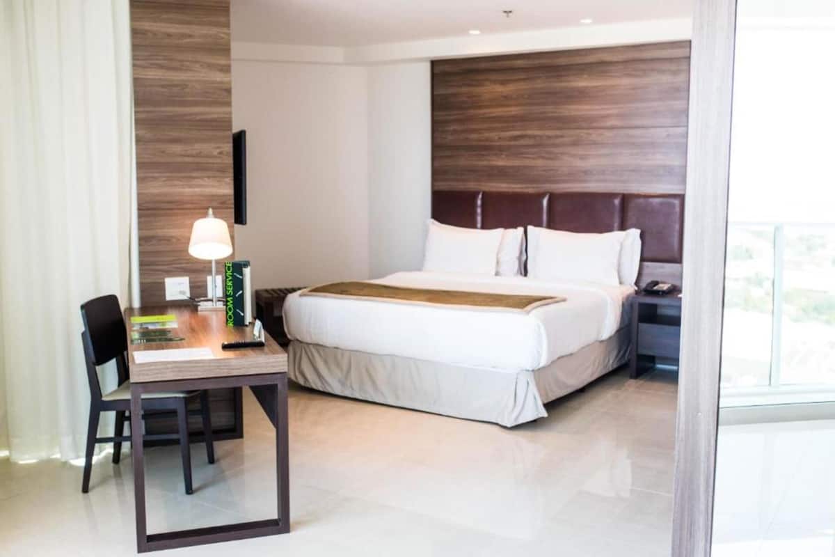 A hotel room with a bed, a desk with a lamp, and a chair.