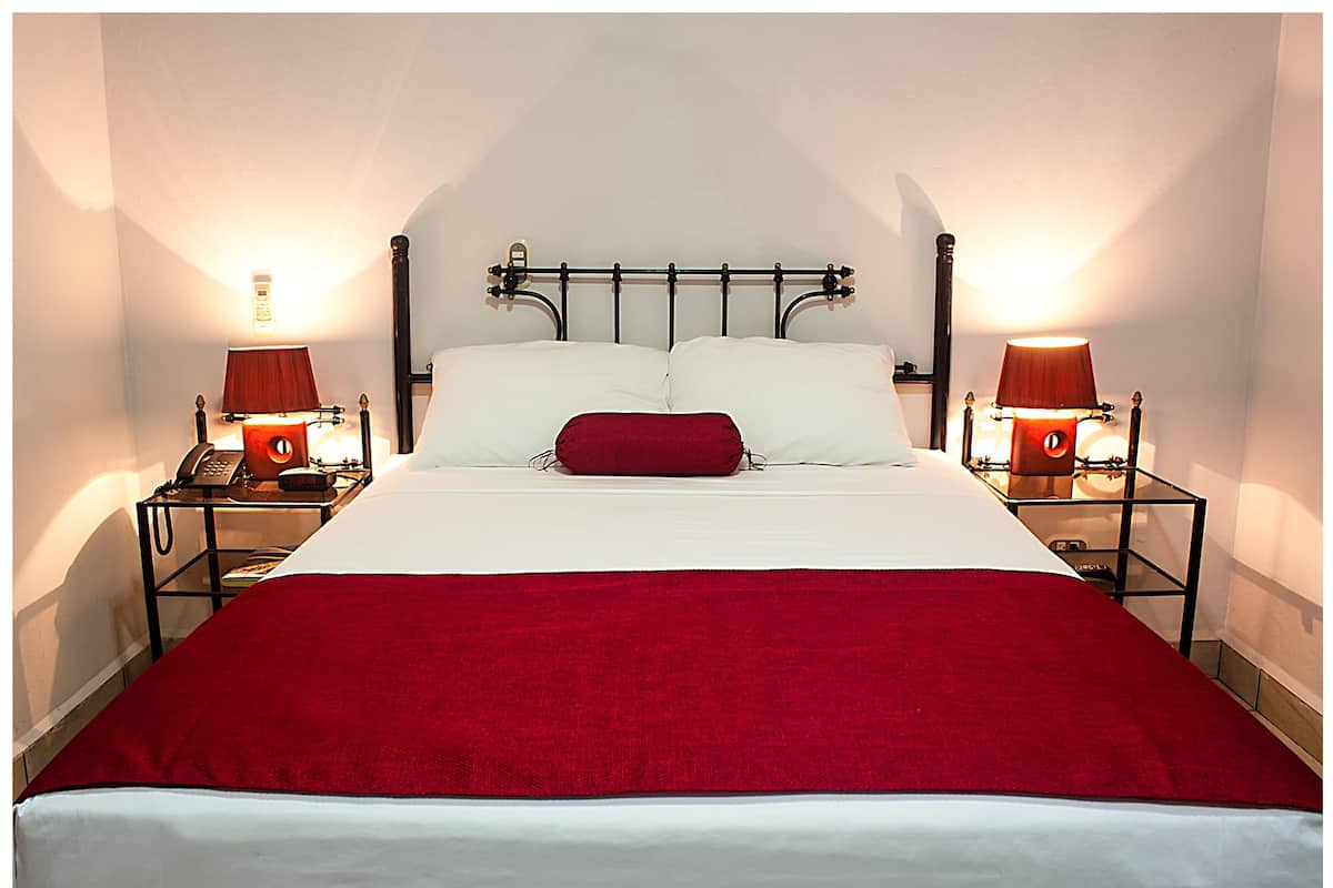 A neatly made bed with a red blanket, two bedside lamps, and a telephone on a bedside table.