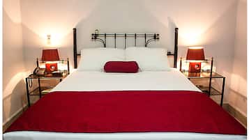 Una cama bien hecha con una manta roja, dos lámparas de noche y un teléfono sobre una mesita de noche.