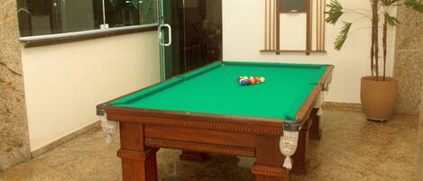 A pool table with balls, a potted plant, and a window with a view.