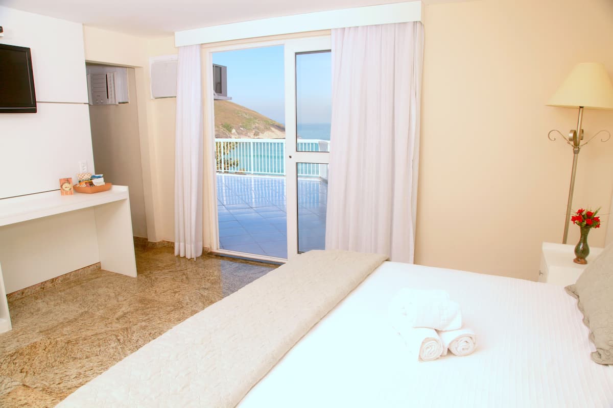 Habitación de hotel con cama, escritorio, televisión, balcón y vista al mar, además de una lámpara.