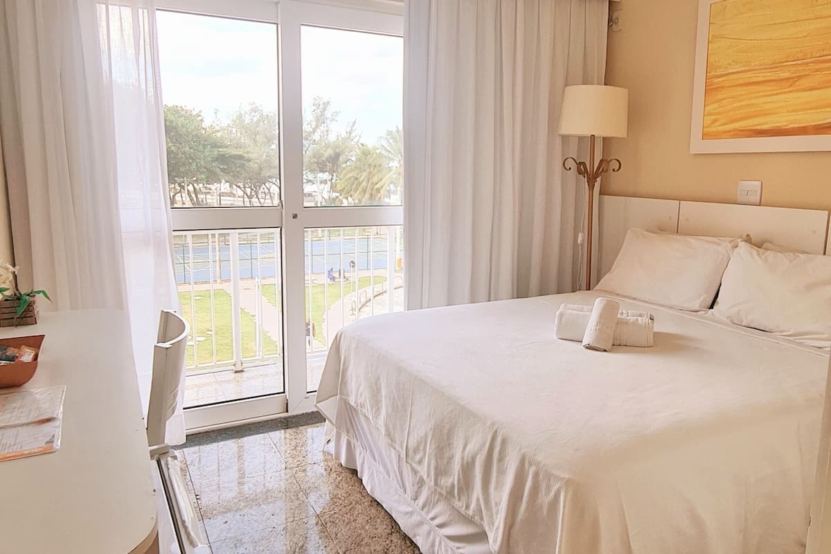 Habitación de hotel con cama, escritorio, lámpara y vista a una cancha de tenis por la puerta.