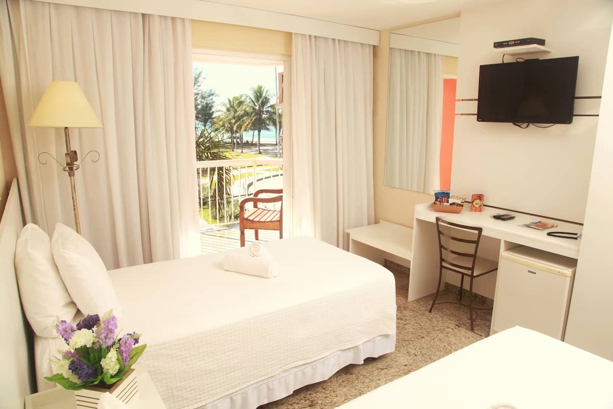 Habitación de hotel con cama, escritorio, silla, televisor y vista a la playa.