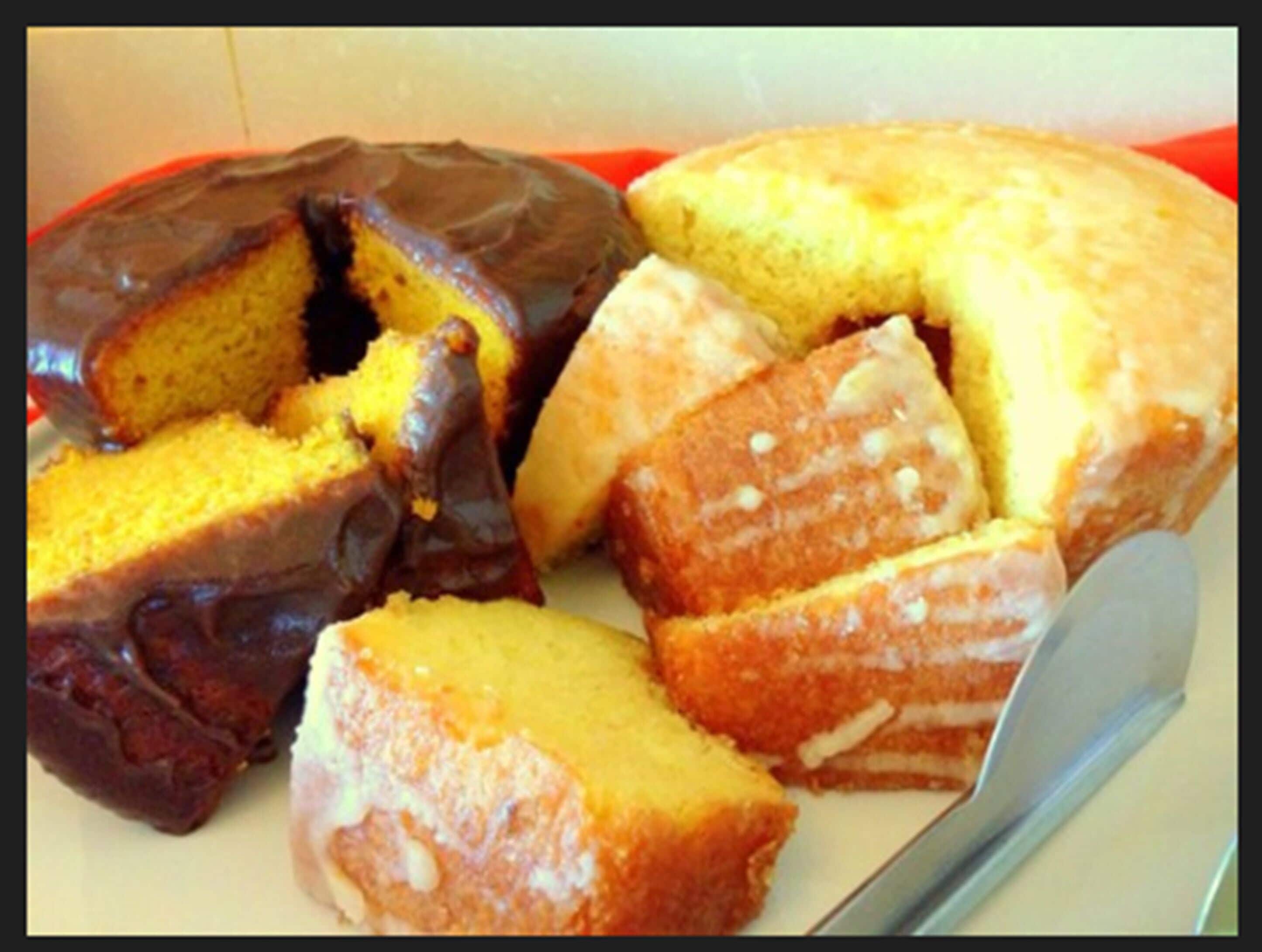 A cake with a chocolate glaze and a yellow sponge, cut into pieces on a plate.