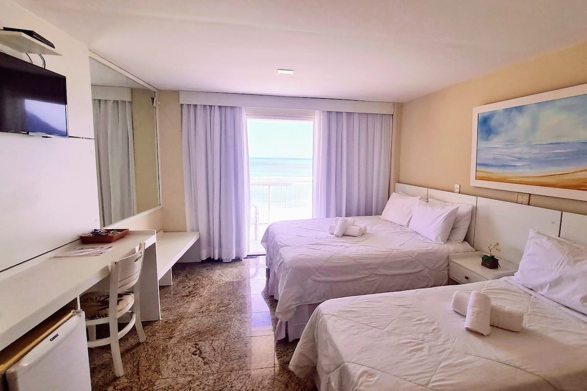 Habitación de hotel con dos camas, un escritorio, un televisor y vista al océano.