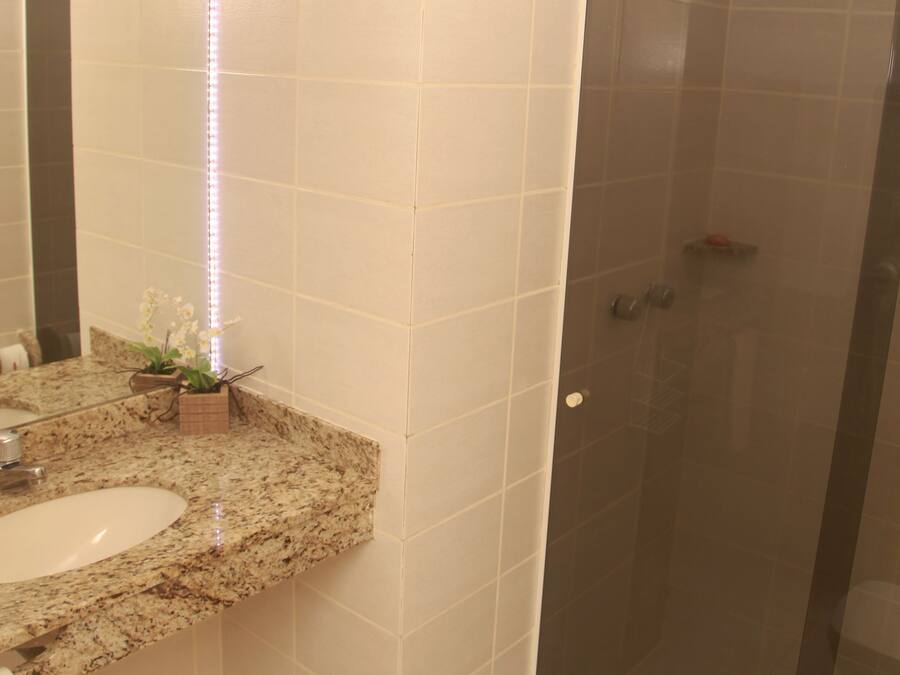 A bathroom with a granite countertop sink, a glass shower enclosure, and a mirror with LED lighting.