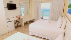 Een hotelkamer met een bed, een bureau, een stoel, een televisie en uitzicht op de oceaan.