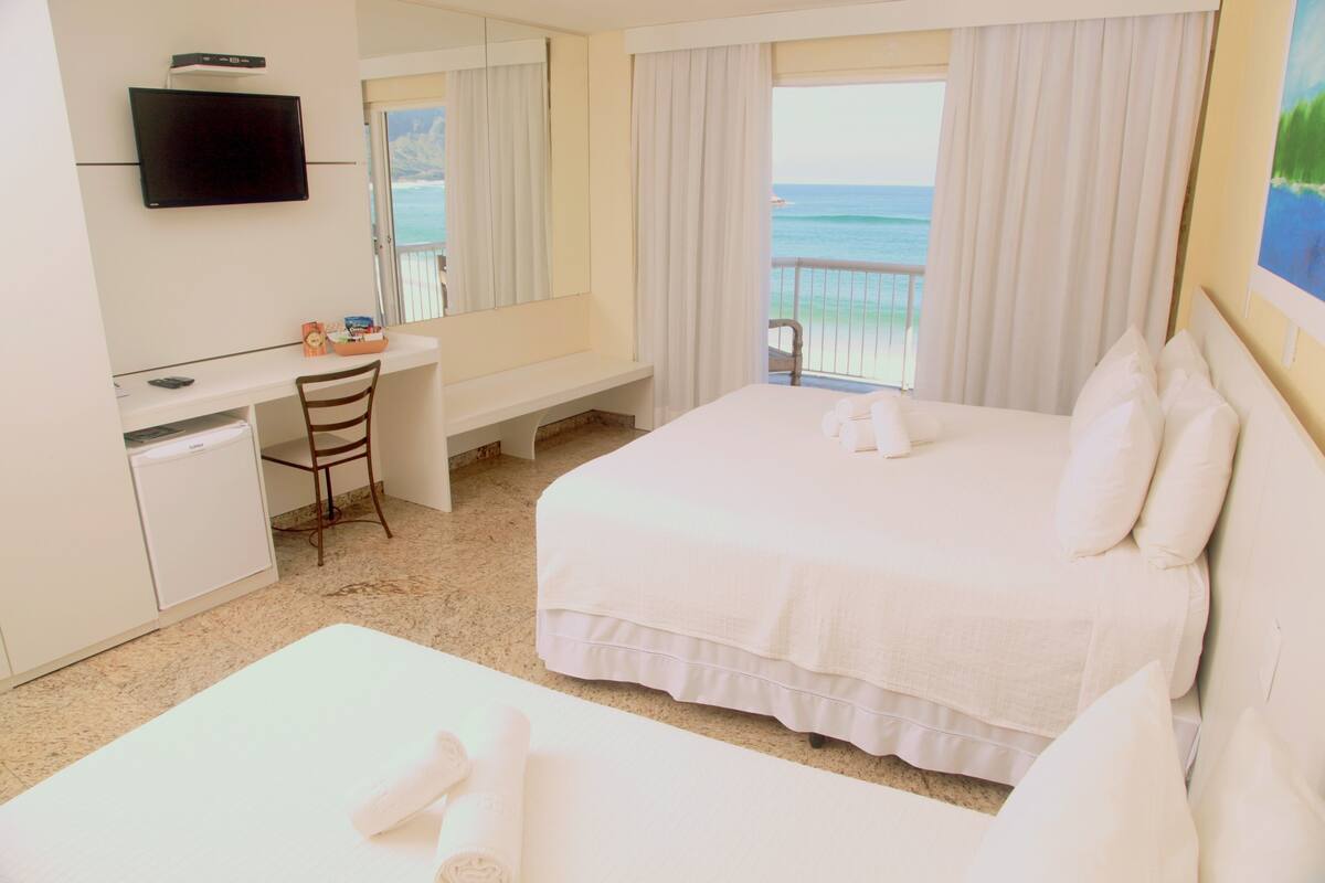Habitación de hotel con cama, escritorio, silla, televisión y vista al océano.