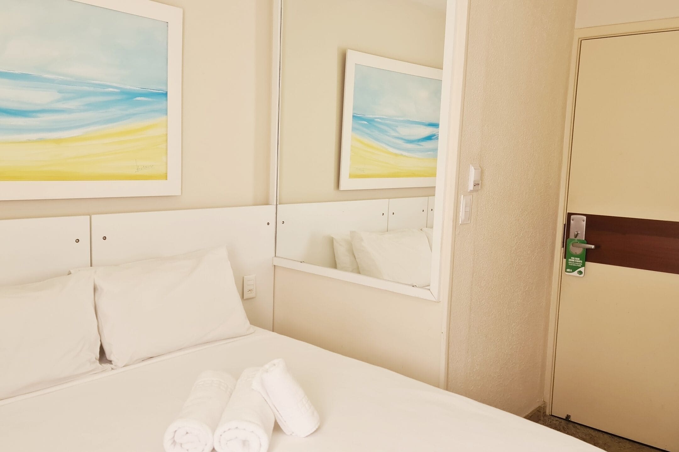 Una camera d'albergo con un letto, due quadri, uno specchio e una porta con serratura.