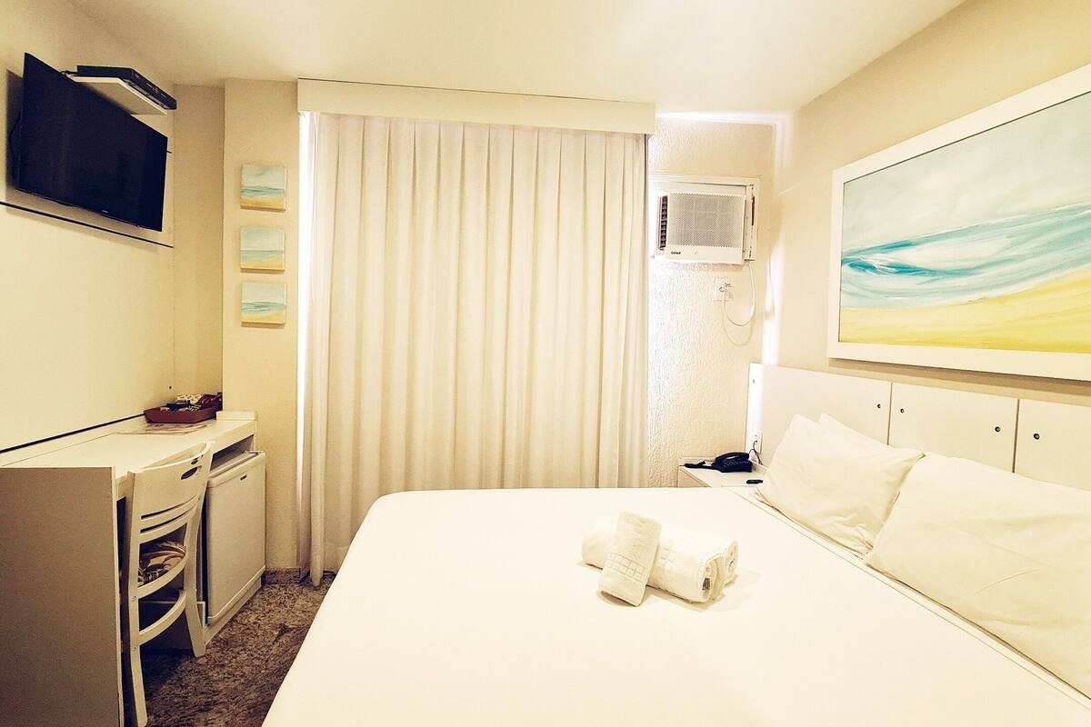 Habitación de hotel con cama, escritorio, televisor, equipo de aire acondicionado y un cuadro en la pared.