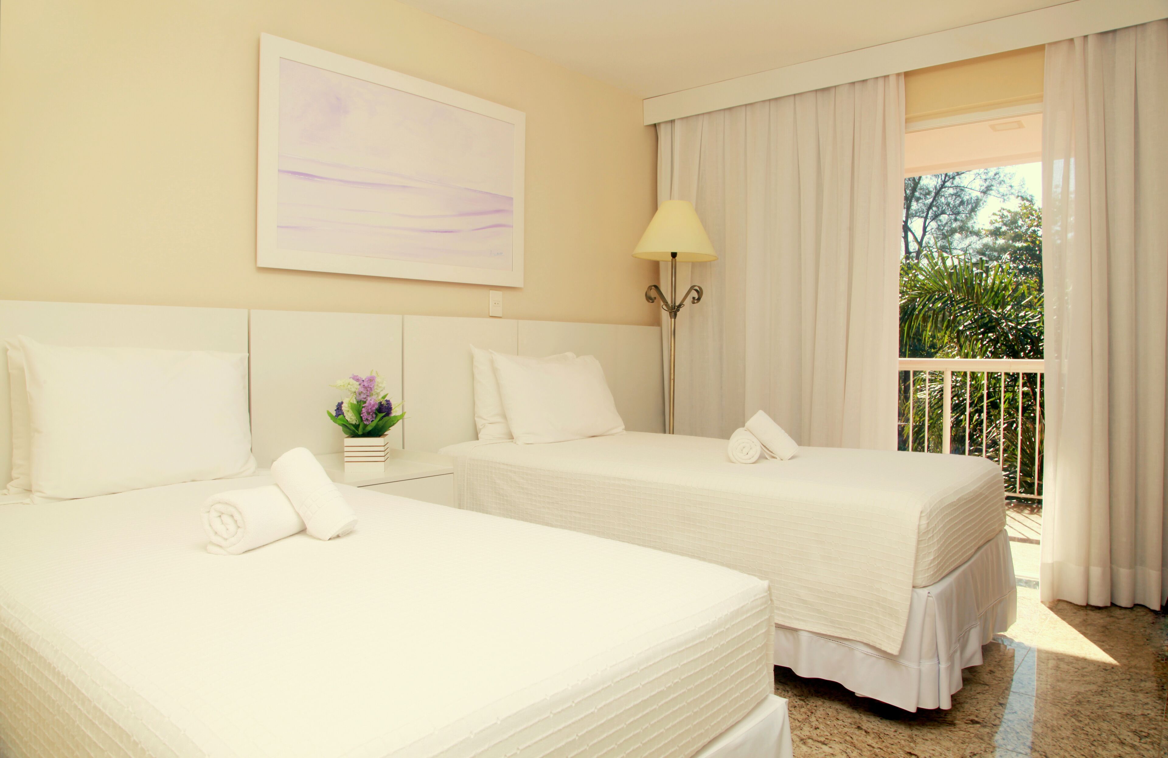 Habitación de hotel con dos camas, un cuadro en la pared, una lámpara y vistas a zonas verdes por la ventana.