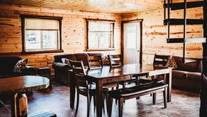 A wooden cabin interior with a dining table, chairs, benches, and a sofa.