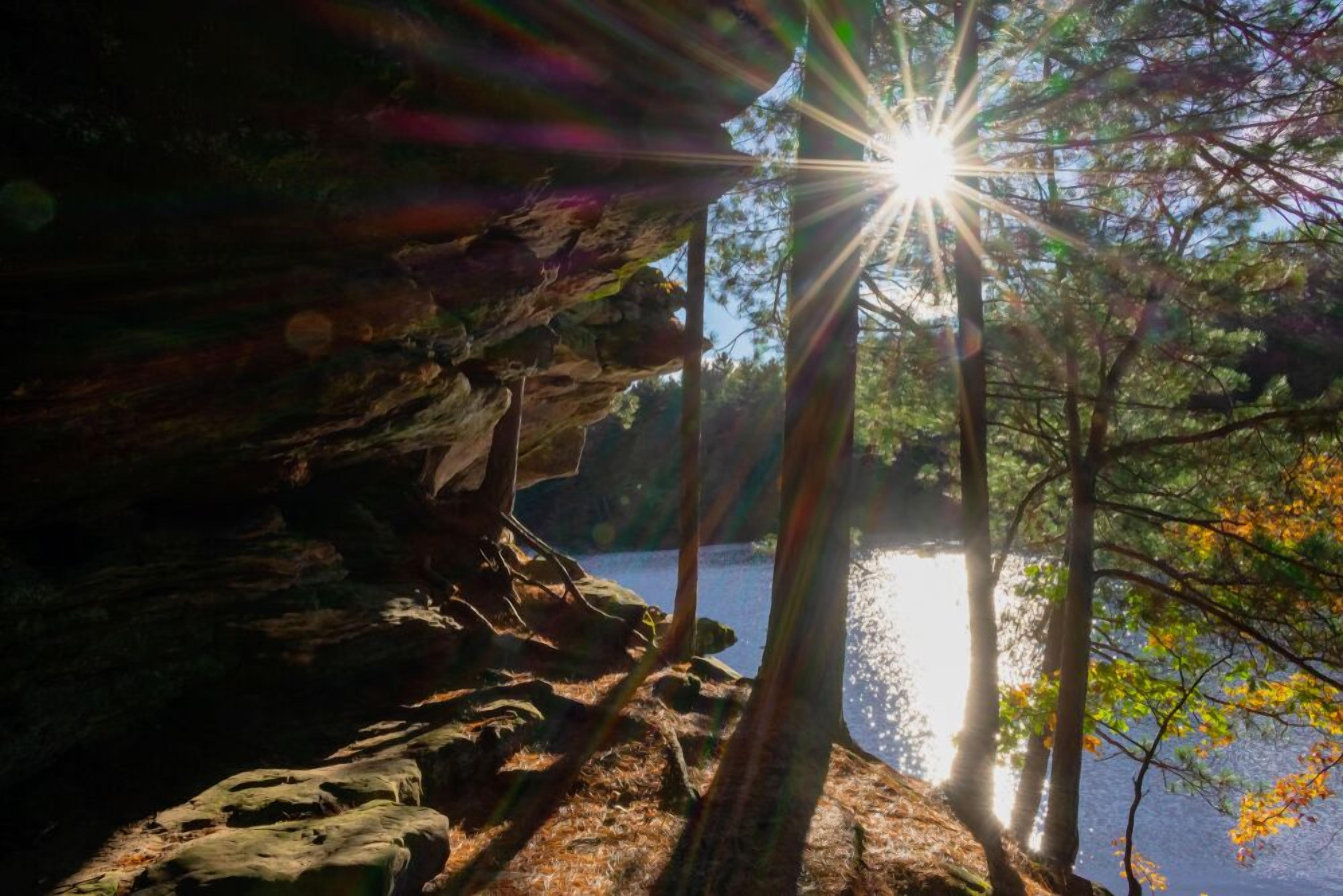 Un paisaje natural con un acantilado rocoso y una masa de agua que refleja la luz del sol.