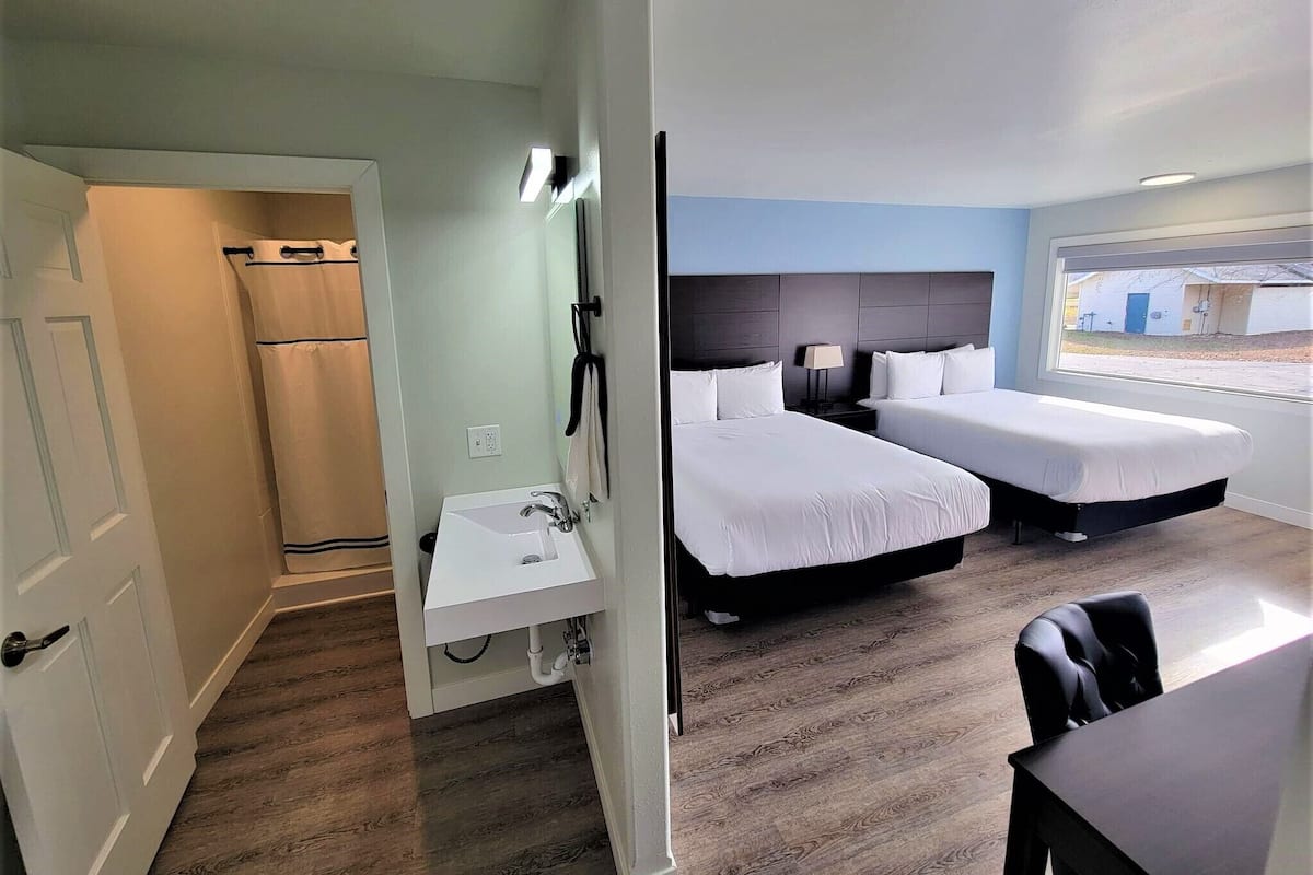 A hotel room with two beds, a small sink, and a window with a view of the outside.