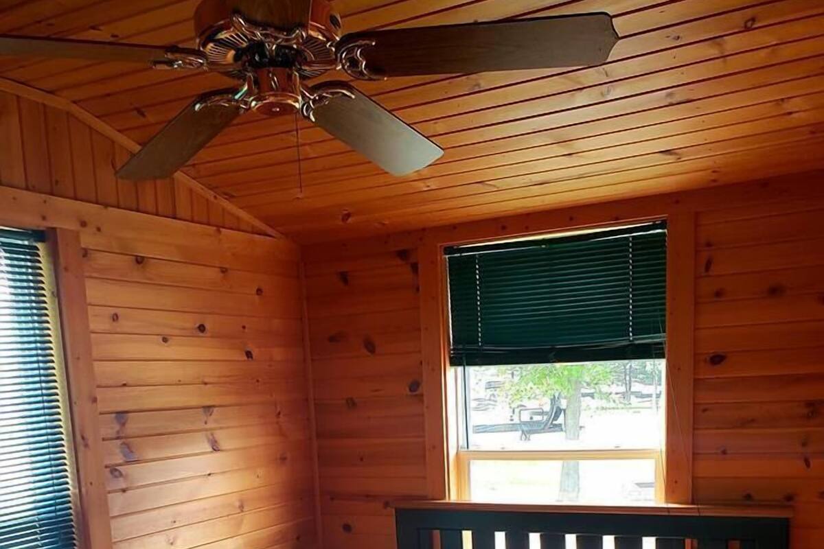 A wooden cabin bedroom with a bed, a window with blinds, and a ceiling fan.