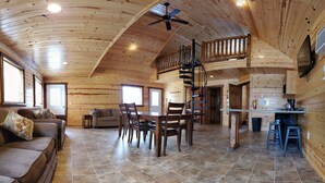 A spacious wooden interior with a dining area, a sofa, a staircase, and a kitchen area.