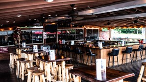 A restaurant with wooden tables and stools, a bar area, and a large window with a view of the outdoors.