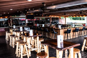 A restaurant with wooden tables and stools, a bar area, and a large window with a view of the outdoors.