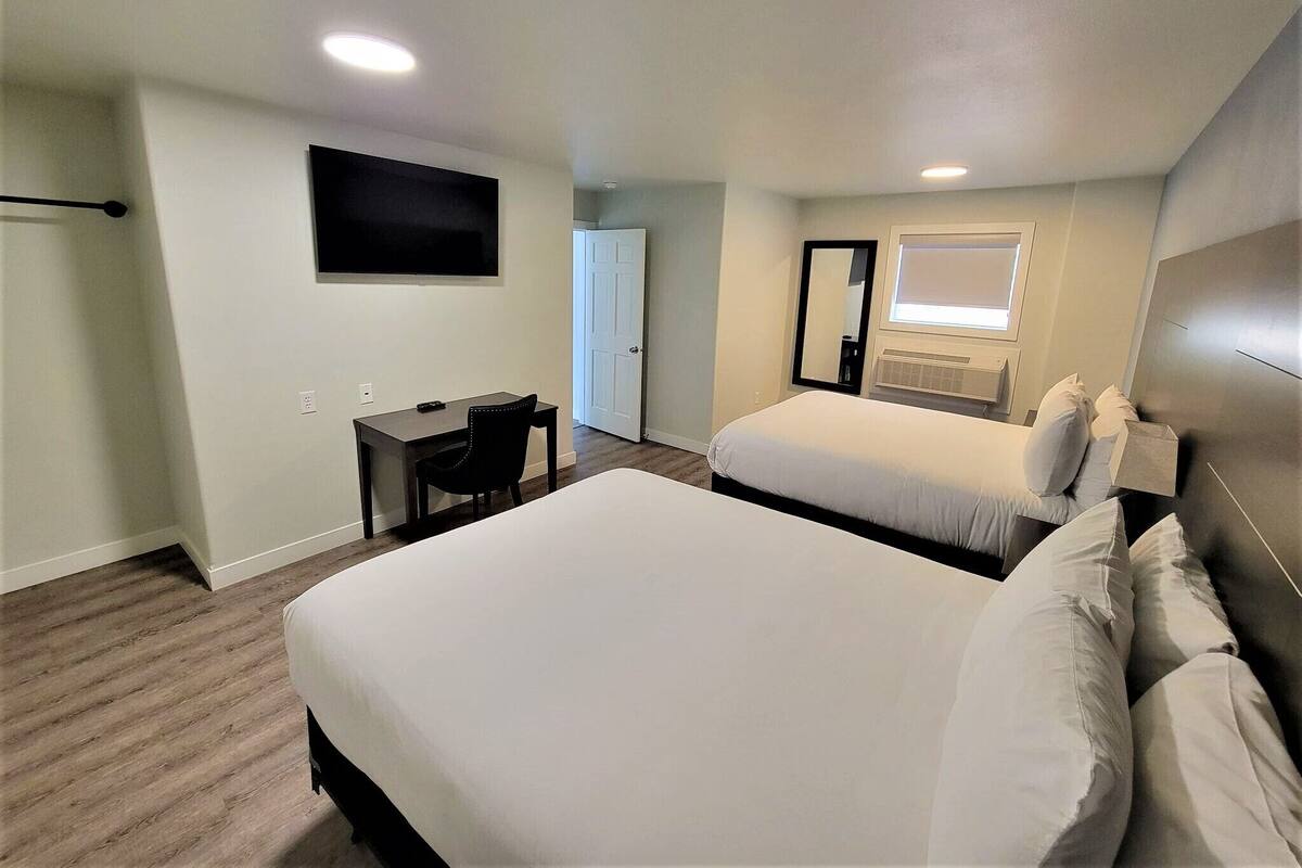 A hotel room with a large bed, a desk, a chair, a TV mounted on the wall, a window, and a door.