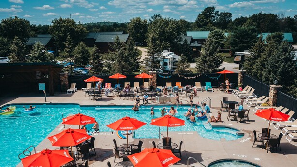 A pool area with multiple red umbrellas, lounge chairs, and a hot tub.