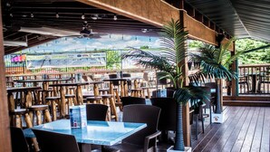 An outdoor restaurant with wooden tables and chairs, a covered seating area, and potted plants.